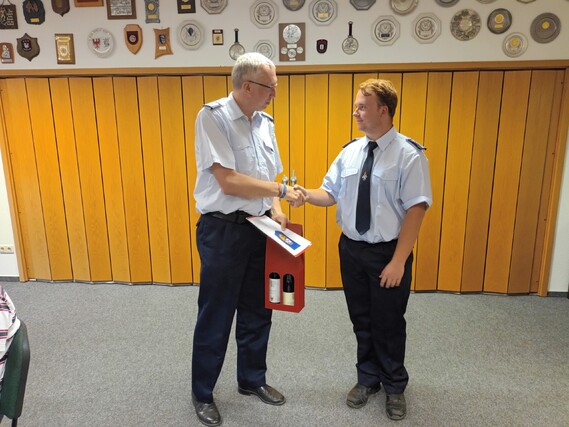 Kreis&shy;jugend&shy;feuerwehrwart Stefan Kothe (links) bedankt sich bei Benjamin Stichling für die geleistete Arbeit als Fachbereichleiter Jugendforum und überreicht die Abberufungsurkunde sowie ein Dankeschöngeschenk.