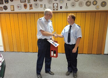 Kreis&shy;jugend&shy;feuerwehrwart Stefan Kothe (links) bedankt sich bei Benjamin Stichling für die geleistete Arbeit als Fachbereichleiter Jugendforum und überreicht die Abberufungsurkunde sowie ein Dankeschöngeschenk.