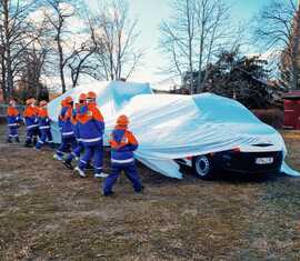 Mitglieder der Jugendfeuerwehren des Amtes Döbern-Land enthüllen ihr neues Mannchaftstransportfahrzeug mit Anhänger.