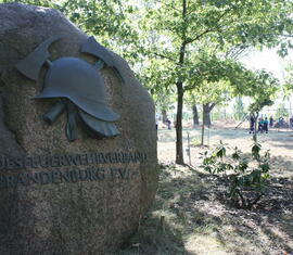 Gedenkstein auf dem Ehrenhain mit dem Schriftzug des Landesfeuerwehrverbandes Brandenburg, im Hintergund noch einer Teilnehmer bei der Reinigung des Ehrenhains